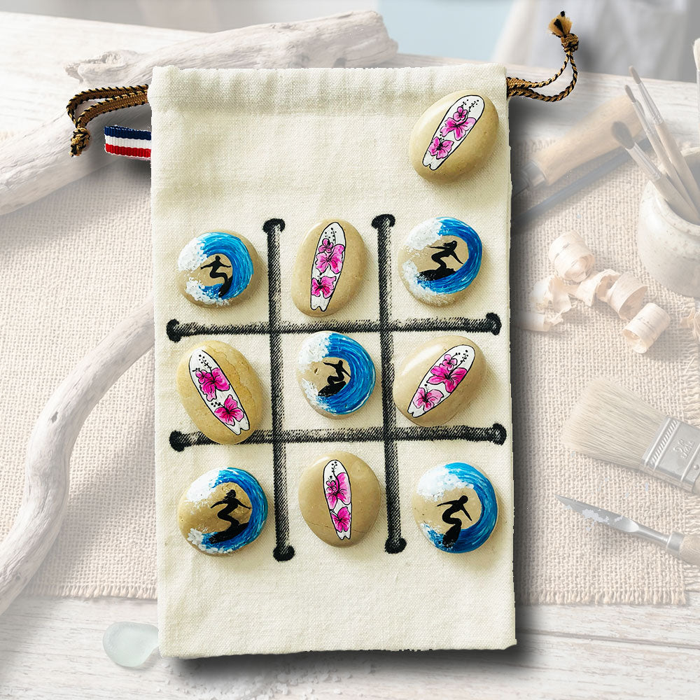 Jeu de morpion sur galets peints, motifs surfeurs bleus et hibiscus roses, sachet en toile beige avec plateau de jeu, artisanat L'Atelier du Ressac.