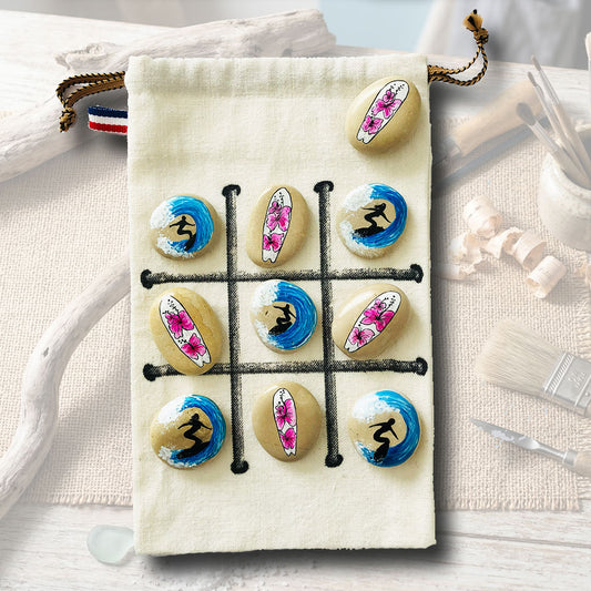 Jeu de morpion sur galets peints, motifs surfeurs bleus et hibiscus roses, sachet en toile beige avec plateau de jeu, artisanat L'Atelier du Ressac.