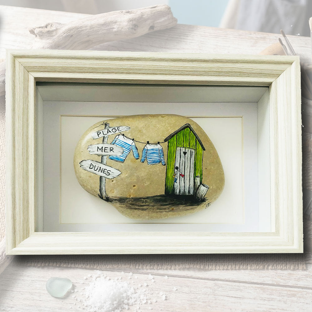 Galet naturel peint à la main représentant une scène de bord de mer avec cabane verte et marinières, cadre coffret bois blanc 15x21cm, artisanat d'art Auvergne L'Atelier du Ressac.