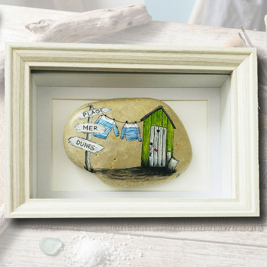 Galet naturel peint à la main représentant une scène de bord de mer avec cabane verte et marinières, cadre coffret bois blanc 15x21cm, artisanat d'art Auvergne L'Atelier du Ressac.
