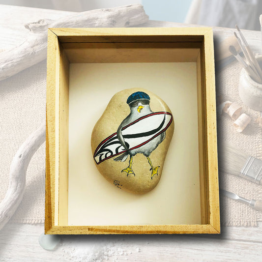 Galet peint à la main, mouette avec bonnet bleu et planche de surf, mis sous cadre bois naturel, création artisanale L'Atelier du Ressac, Auvergne.